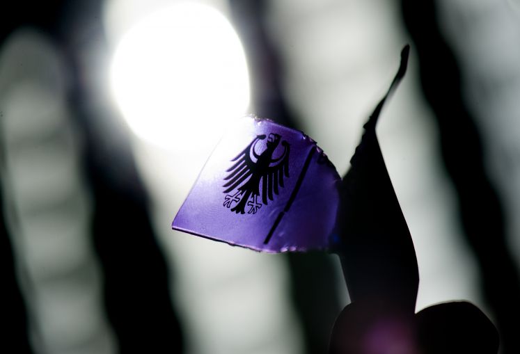 Der Bundesadler, das Bundeswappen der Bundesrepublik Deutschland, mit einem Fingerabdruck auf einem zerrissenen Armband