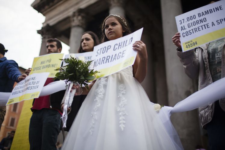 Ein Mädchen hält bei einer Protestaktion im Brautkleid dein Schild in der Hand. Die Aufschrift: Stop child marriage