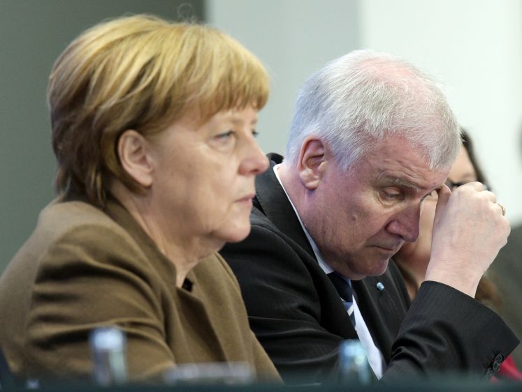 Angela Merkel und Host Seehofer sitzen nebeneinander. Seehofer runzelt die Stirn und fasst sich mit dem Daumen an die Augenbraue.