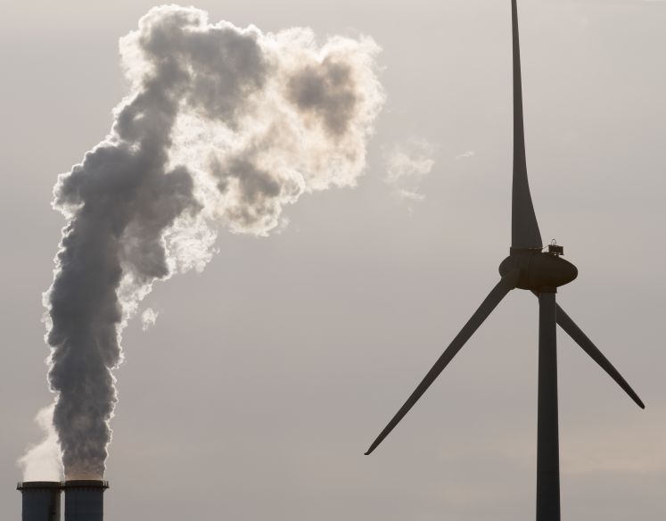 Der rauchende Schlot eines Kohlekraftwerks neben einem Windrad