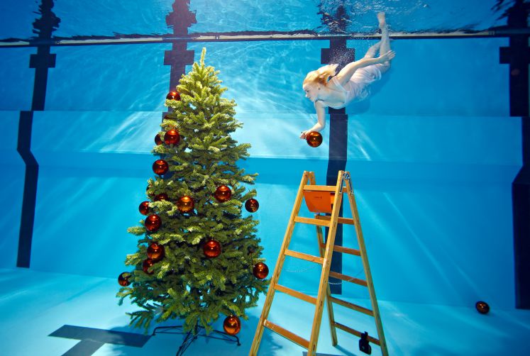 Eine als Engel verkleidete Taucherin hängt eine Kugeln an einen in einem Schwimmbad-Becken stehenden Weihnachtsbaum.