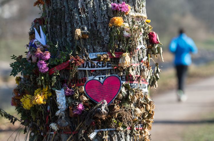 Ein Polizeiabsperrband ist um einen Baum gewickelt. Passanten klemmten in das Absperrband Blumen.