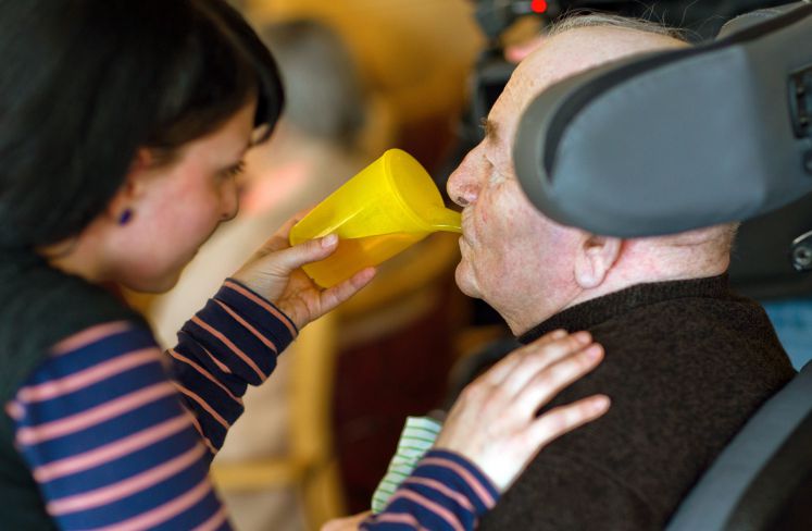 Eine Altenpflegerin hilft einem Pflegebedrüftigen beim Trinken.