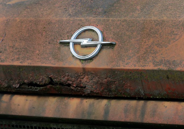 Eine rostige Motorhaube eines Opel-Fahrzeugs mit dem Blitzemblem 