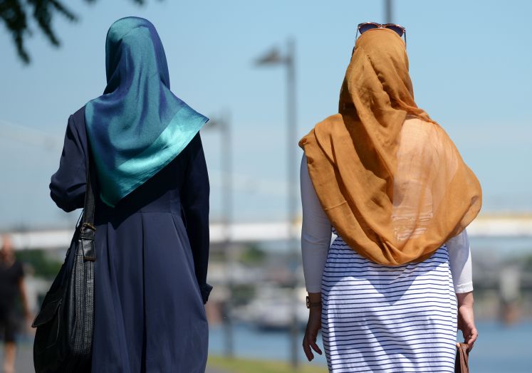 Zwei Frauen mit Kopftuch spazieren in der Sonne.