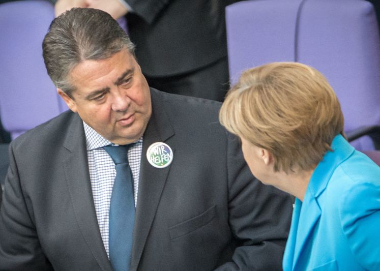 Sigmar Gabriel, den "Wir helfen"-Button am Revers, spricht mit Angela Merkel