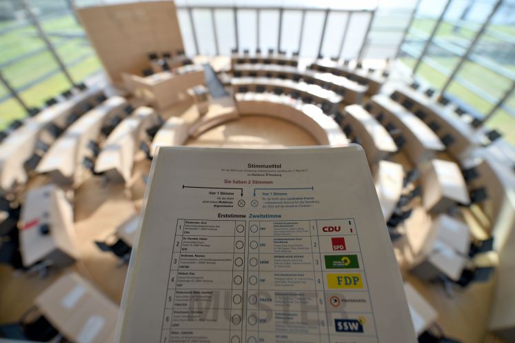 Ein Stimmzettel und im Hintergrund ein Parlamentsraum