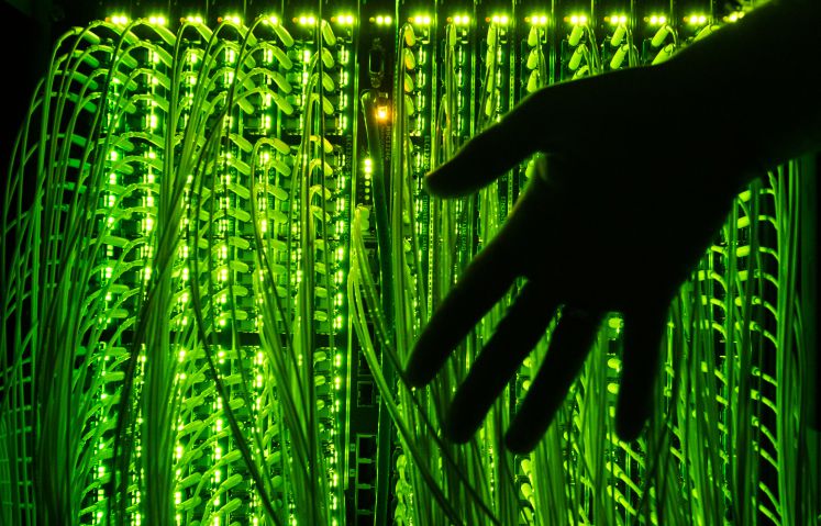 Ein Mann hält seine Hand vor einen Verteilerpunkt, in dem zahlreiche Glasfaserkabel zusammenlaufen