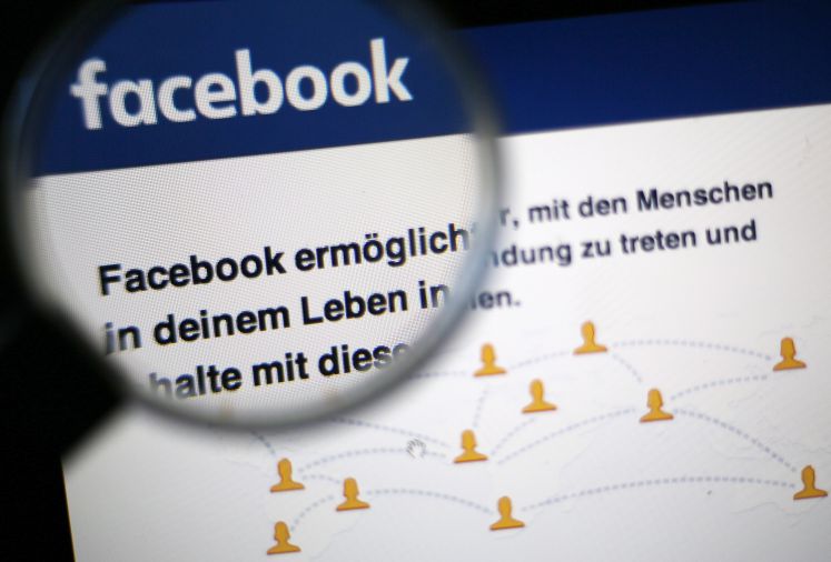 Die Startseite von Facebook wird teilweise durch eine Lupe betrachtet