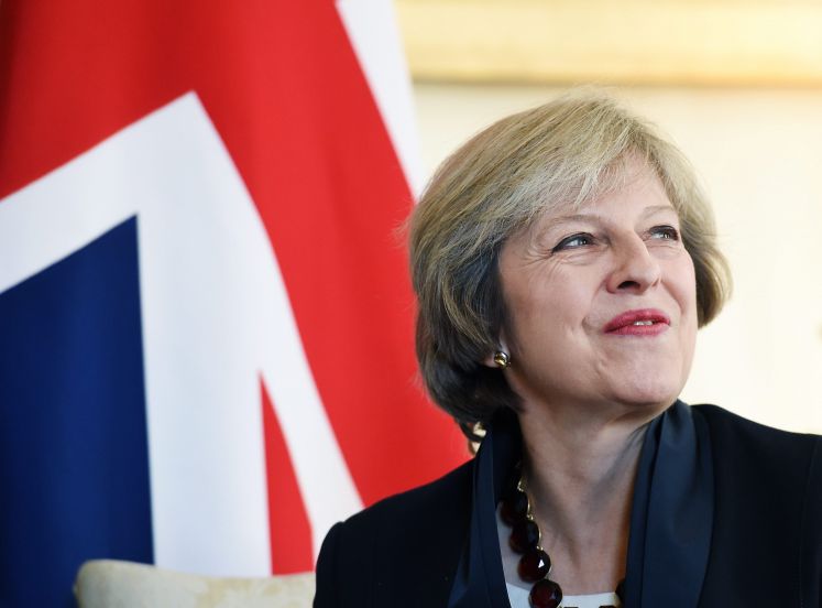 Theresa May lächelt. Hinter ihr die britische Flagge