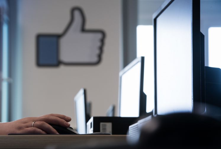 Eine Mitarbeiterin bedient am 10.07.2017 bei einem Pressetermin im Löschzentrum von Facebook in einem Service-Center in Berlin die Maus eines Computers. An der Wand des Großraumbüros steht das Logo für den Like-Daumen bei "Facebook".