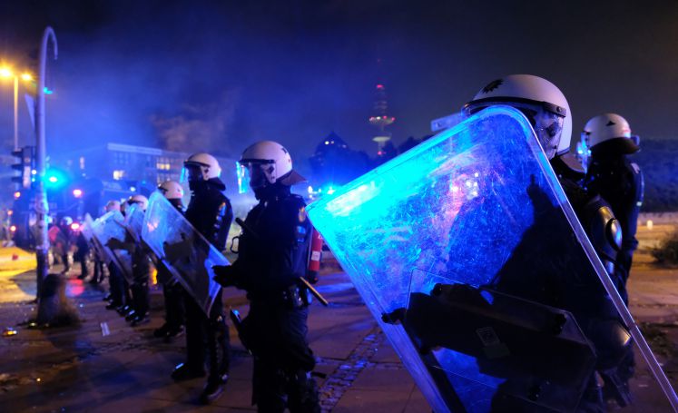 Polizisten stehen mit Schild und Schlagstöcken in einer Reihe und sichern während des G20-Protest eine Straße