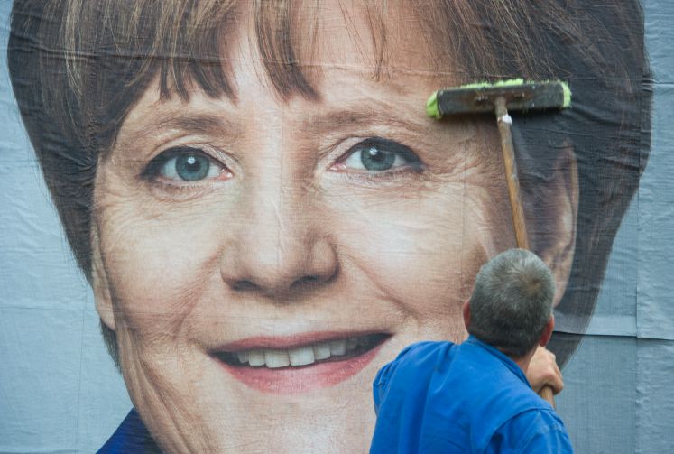 Ein Mann klebt am 09.05.2014 in Stralsund (Mecklenburg-Vorpommern) ein Wahlplakat zum Europawahlkampf mit Bundeskanzlerin Angela Merkel (CDU) auf eine Stellwand