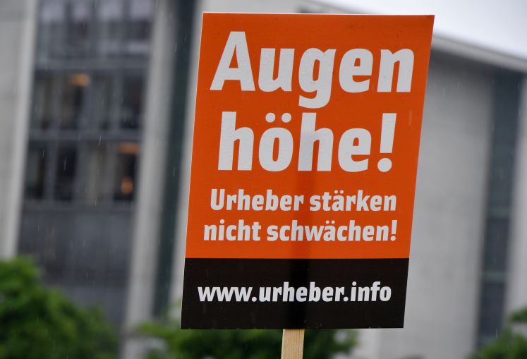 Künstler und Urheber protestieren gegen die Reform des Urheberrechts. Man sieht ein Schild mit der Aufschrift "Augenhöhe - Urheber stärken, nicht schwächen!"