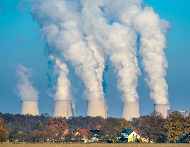Neben einem malerischen Dorf im Wald entlässt ein riesiges Braunkohlekraftwerke Wasserdampf in die Luft