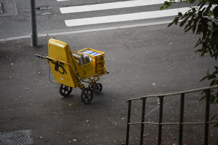 Ein einsamer Trolley der Deutschen Post steht in Stuttgart vor einem Haus.