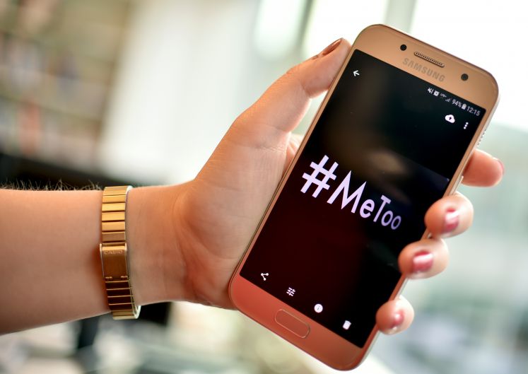 Eine junge Frau hält ein Smartphone mit dem Hashtag "#MeToo" in der Hand