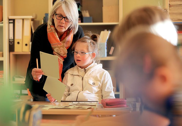 Eine Lehrerin betreut in einer Gemeinschaftsschule ein Mädchen mit Down-Syndrom