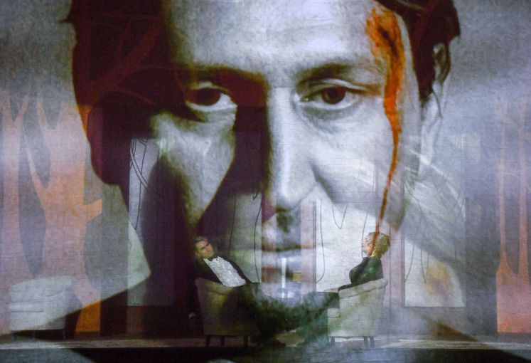 Die Sänger Andreas Schager und Anja Kampe hinter einem transparenten Vorhang, auf dem Videobilder zu sehen sind