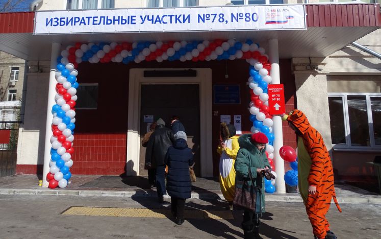 Ein Mann in einem Tigerkostüm spricht mit Wählern vor einem russischen Wahllokal