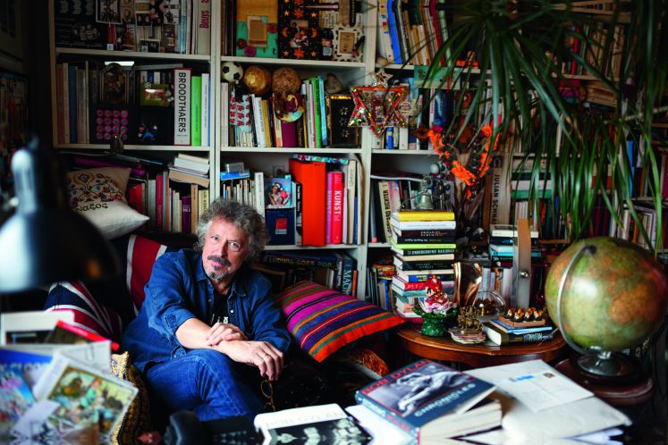 Wolfgang Niedecken sitzt in seiner Bibliothek auf einem Sofa vor einem großen Bücherregal