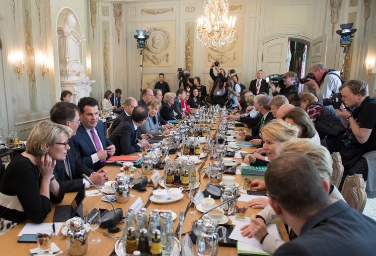 Die Mitglieder des neuen Bundeskabinetts sitzen im Schloss Meseberg an einem Tisch. 