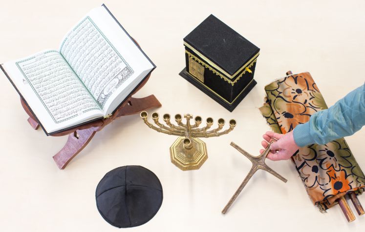Symbole der drei Religionen Islam, Judentum und Christentum (Koran mit Koranständer (l-r), Kippa Kopfbedeckung, Chanukkaleuchter, Kaaba "Würfel", Kreuz und Torarolle) liegen am 23.11.2017 auf einem Tisch der Drei-Religionen-Schule in Osnabrück (Niedersachsen).