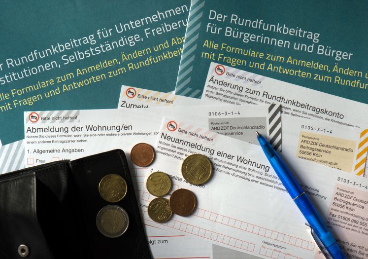 ILLUSTRATION - Auf einem Tisch in einem Büro in Dresden (Sachsen) liegt am 15.04.2016 eine offene Geldbörse mit Münzgeld auf Formularen für Bürgerinnen und Bürger, Unternehmen, Institutionen, Selbstständige und Freiberufler zu den Rundfunkbeiträgen ARD, ZDF und DRadio
