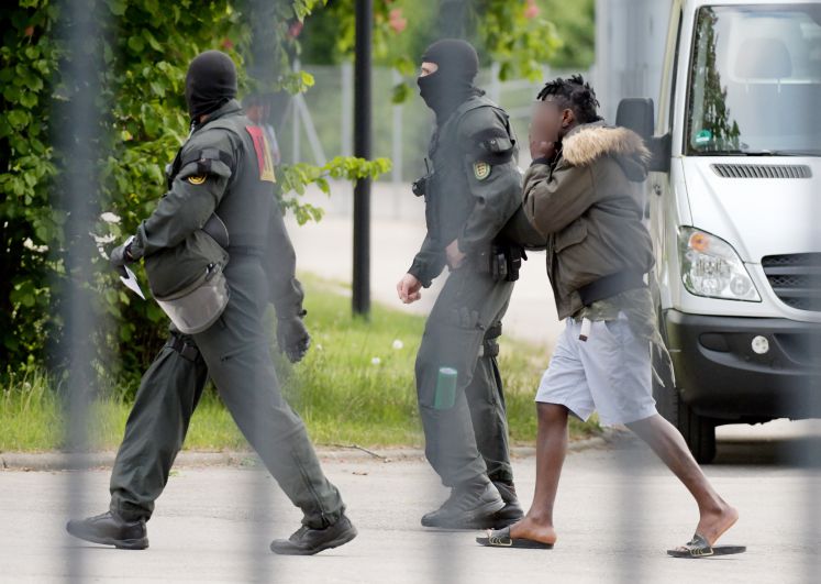 In der Landeserstaufnahmeeinrichtung für Flüchtlinge (LEA) wird ein Mann von maskierten Polizisten eskortiert. Nachdem es bei der gescheiterten Abschiebung eines 23-jährigen Togolesen vor vier Tagen zu Ausschreitungen gekommen war, läuft ein Großeinsatz der Polizei in der Flüchtlingsunterkunft. (ACHTUNG: Die Person wurde aus persönlichkeitsrechtlichen Gründen unkenntlich gemacht)