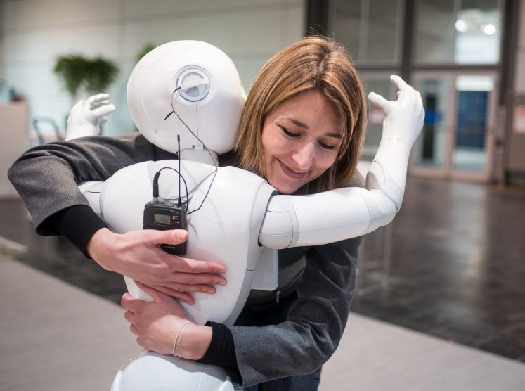 Die Kommunikationsmanagerin von Aldebaran, Aurora Chiquot, umarmt am 13.03.2016 auf dem Messegelände der CeBIT Hannover (Niedersachsen) am Stand von Aldebaran den humanoiden Roboter "Pepper". Foto: Ole Spata/dpa