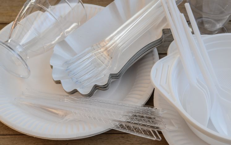 Einweggeschirr aus Pappe und Messer, Gabeln, und Becher aus Plastik liegen zusammen auf einem Tisch.