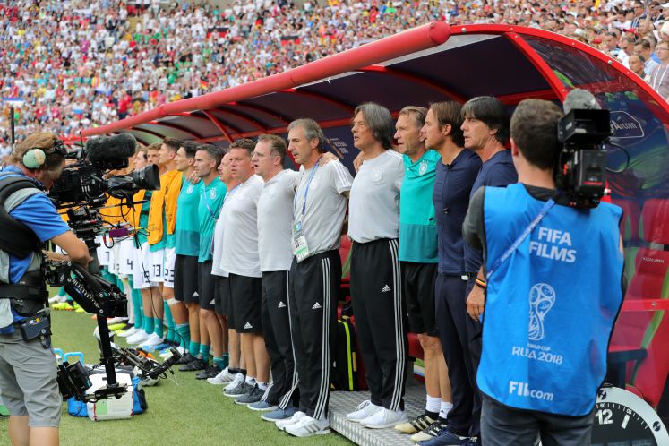 27.06.2018, Russland, Kasan: Fußball: WM, Vorrunde, Gruppe F, 3. Spieltag: Südkorea - Deutschland in der Kasan-Arena. (v.r.) Trainer Joachim Löw aus Deutschland, Assistenztrainer Thomas Schneider aus Deutschland, Torwarttrainer Andreas Köpke aus Deutschland, Mannschaftsarzt Hans-Wilhelm Müller-Wohlfahrt, Mannschaftsarzt Hans-Dieter Hermann, Mannschaftsarzt Tim Meyer, Physiotherapeut Christian Huhn stehen bei der Nationalhymne zusammen vor der Bank. 