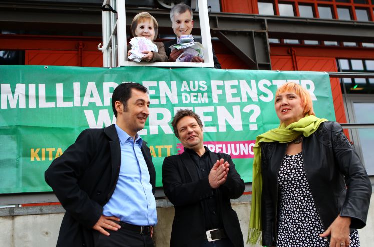 Die Bundesvorsitzenden der Grünen, Claudia Roth (r) und Cem Özdemir (l), sowie der Spitzenkandidat für die Landtagswahlen in Schleswig-Holstein, Robert Habeck (M) beobachten am Samstag (28.04.2012) in Lübeck am Rande des Länderrats eine Aktion, bei der im Hintergrund symbolisch Bundeskanzlerin Merkel und CSU-Chef Seehofer Geld aus dem Fenster werfen. Mit Konzepten für die Energiewende und eine gerechte Finanzpolitik wollen die Grünen auf dem kleinen Parteitag gegen die schwarz-gelben Koalitionen im Bund und