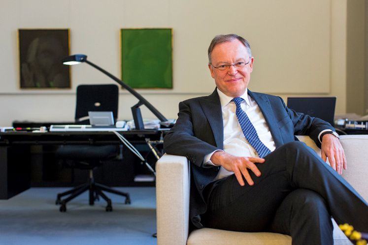 Stephan Weil sitzt in seinem Büro auf einem Sessel und lächelt in die Kamera