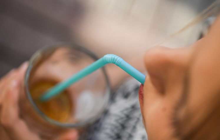 Ein Mädchen trinkt mit einem Strohhalm aus Plastik aus einem Glas.