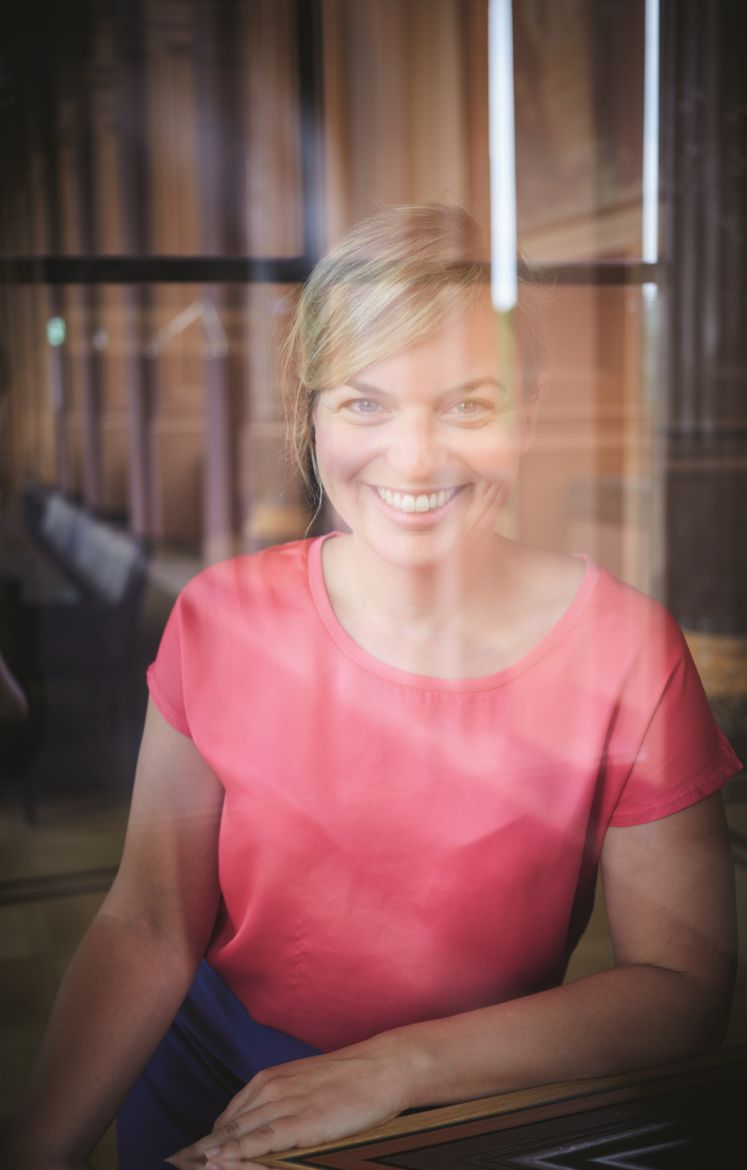 Katharina Schulze in pinkem Top hinter einer Fensterscheibe sitzend und in die Kamera lächelnd