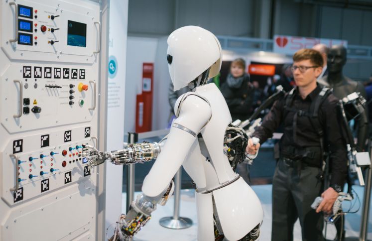 Ein Mitarbeiter des Robotic Innovation Centers steuert am 20.03.2017 bei der CeBIT Messe in Hannover (Niedersachsen) am Stand des deutschen Forschungszentrums für Künstliche Intelligenz (DFKI) mit Hilfe eines Exoskeletts den Roboter AILA.