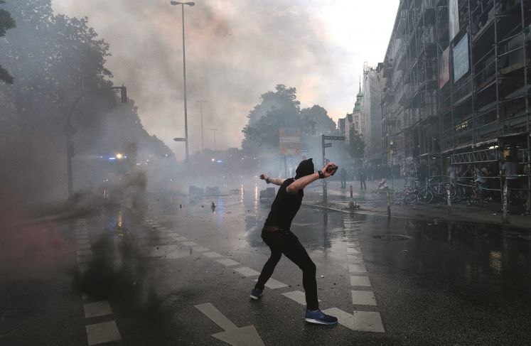 Vermummter Linksextremist wirft während des G20-Gipfels in der Hamburger Sternschanze einen Stein auf die anrückenden Polizisten