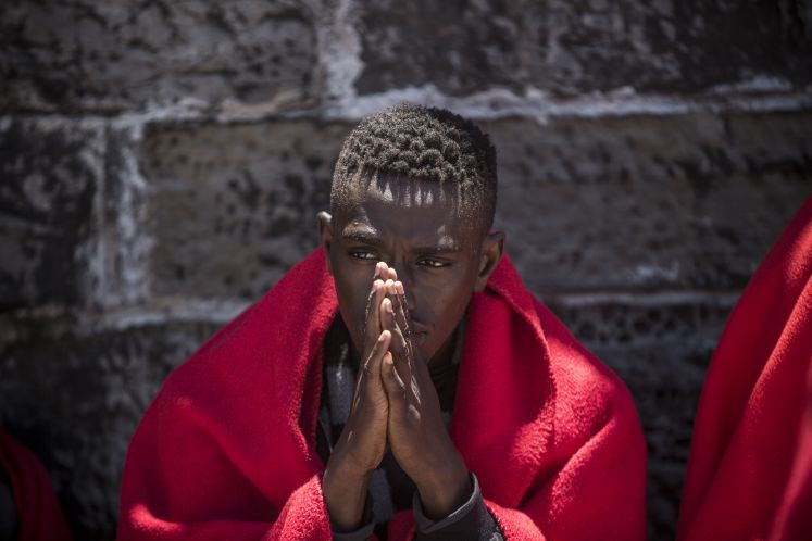 29.06.2018, Spanien, Tarifa: Ein Migrant aus Afrika sitzt nach seiner Rettung in der Straße von Gibraltar im Hafen von Tarifa in eine Decke gehüllt an einer Mauer. Die EU-Staaten haben sich bei ihrem Gipfel in Brüssel darauf geeinigt, in der EU geschlossene Aufnahmelager für gerettete Bootsflüchtlinge einzurichten.
