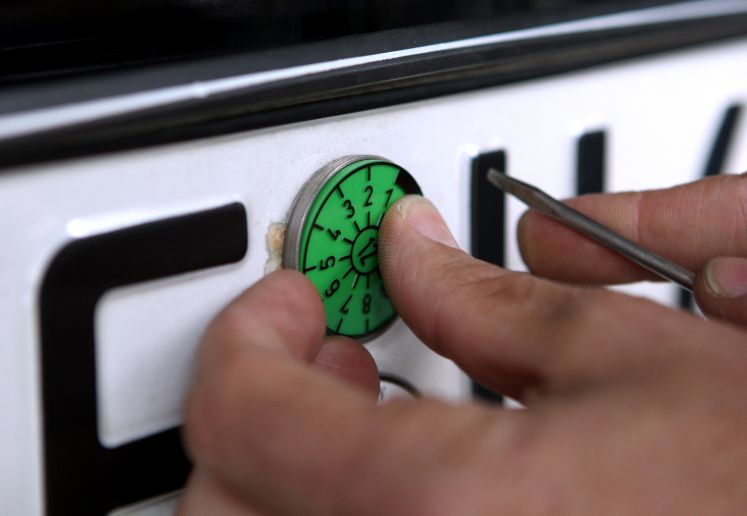 Ein Prüfer des TÜV Bayern befestigt am Montag (03.05.2010) in Kaufbeuren (Schwaben) eine TÜV-Plakette am Kennzeichen eines soeben geprüften Autos.