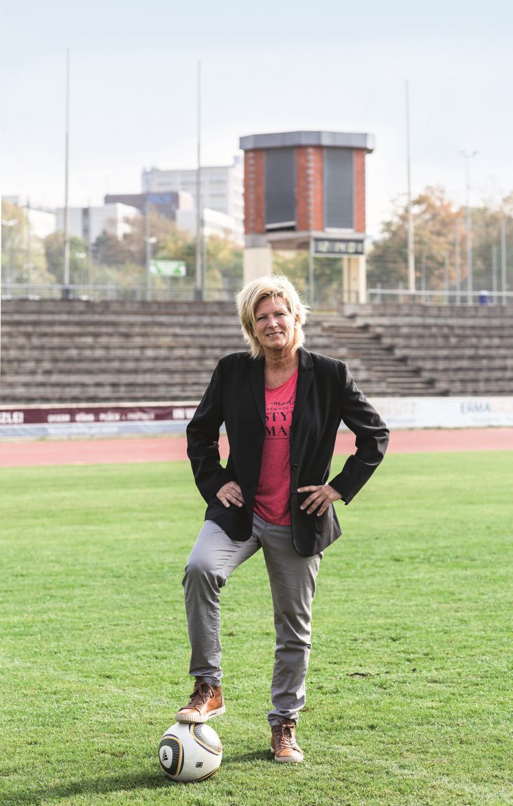 Claudia Neumann auf einem Fußballplatz, unter dem rechten Fuß ein Fußball