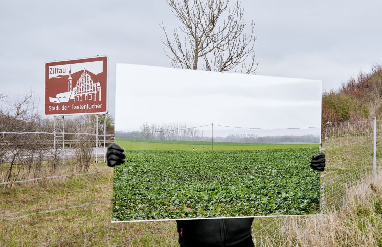 Eine Persion steht an der Europastraße und hält ein Landschaftsbild der Europastraße hoch