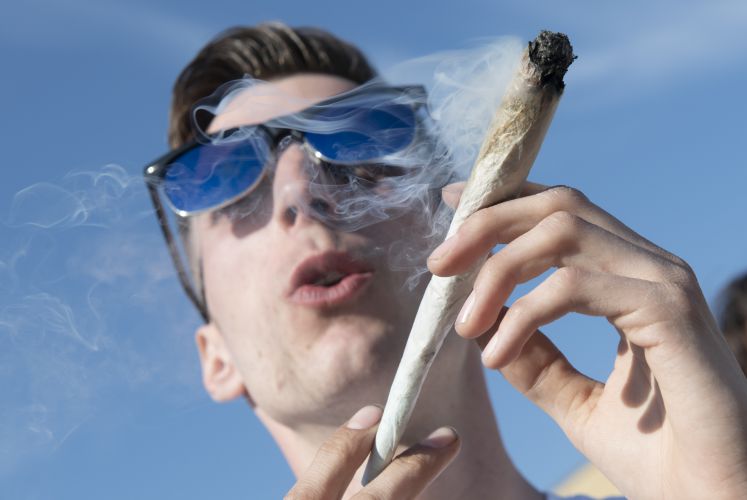 Ein junger Mann aus Berlin raucht aus medizinischen Gründen bei einer Protestaktion für legalen Cannabis-Konsum im Görlitzer Park einen übergroßen Joint.