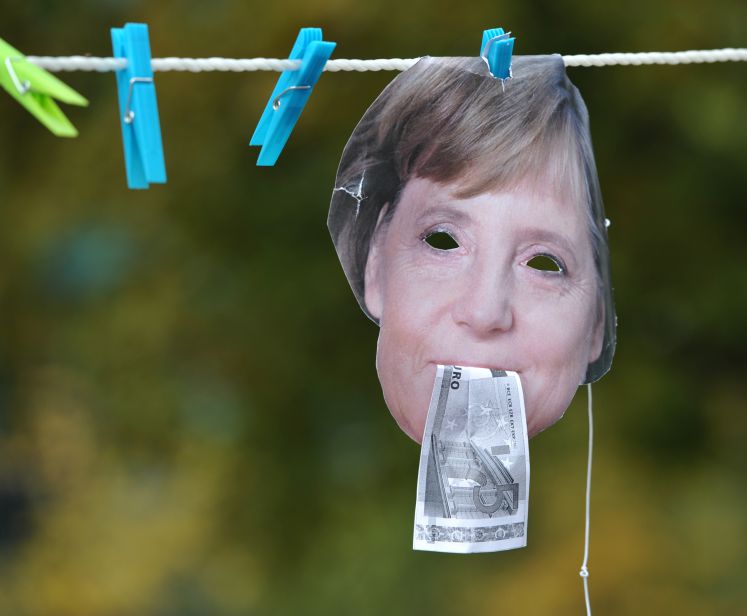 Eine Maske von Merkel mit Geld im Mund