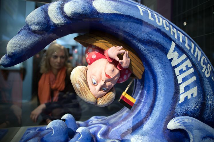 09.10.2018, Nordrhein-Westfalen, Bonn: ILLUSTRATION - Eine Mitarbeiterin des Hauses der Geschichte betrachtet ein das Model eines Karnevalswagen mit dem Motiv Flüchtlingswelle. Die Ausstellung «Angst. Eine deutsche Gefühlslage?» im Haus der Geschichte untersucht die berüchtigte «German Angst» und konzentriert sich dabei auf die Themenkomplexe Zuwanderung, Atomkrieg, Umweltzerstörung und Überwachung.