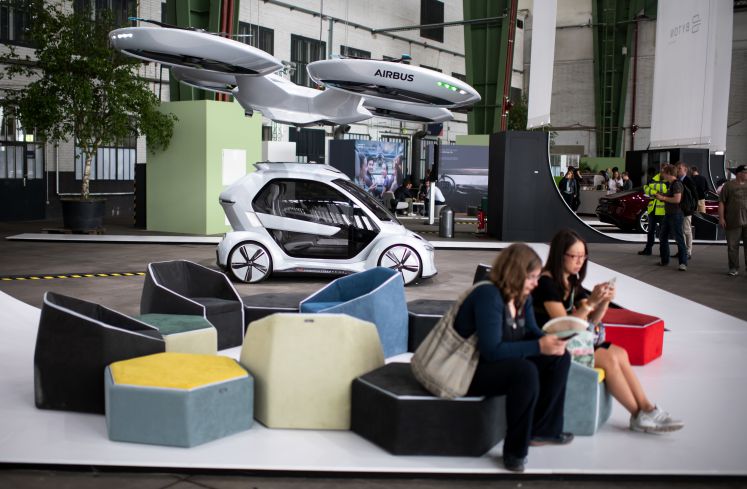 Zwei Besucherinnen sitzen bei der Green Tech Exhibition im Rahmen des Green Tech Festival im Hangar des ehemaligen Flughafen Tempelhof vor dem Modell eines Flug-Autos ("Pop.Up Next"), das von Audi und Airbus zusammen entwickelt wurde.