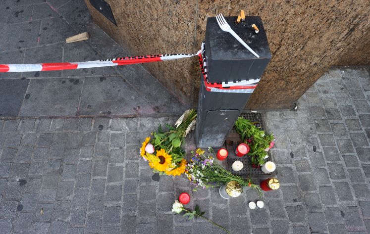 Kerzen und Blumen liegen vor einem geschlossenen und abgesperrten Geschäft in der Innenstadt.