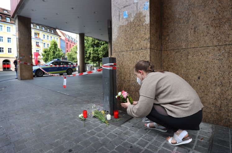 Eine junge Frau legt vor einem geschlossenen und abgesperrten Geschäft in der Innenstadt Blumen ab. 