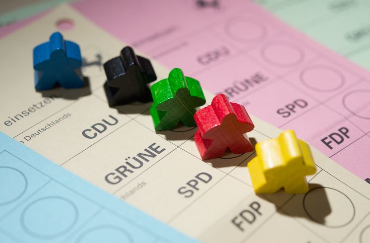 Farbige Spielfiguren stehen auf Wahlscheinen