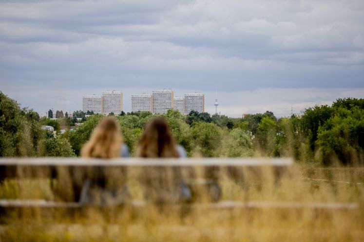Zwei Frauen sitzen auf einer Bank auf dem ehemaligen IGA-Gelände in Berlin-Marzahn mit Sicht auf Plattenbauten und den Berliner Fernsehturm.
